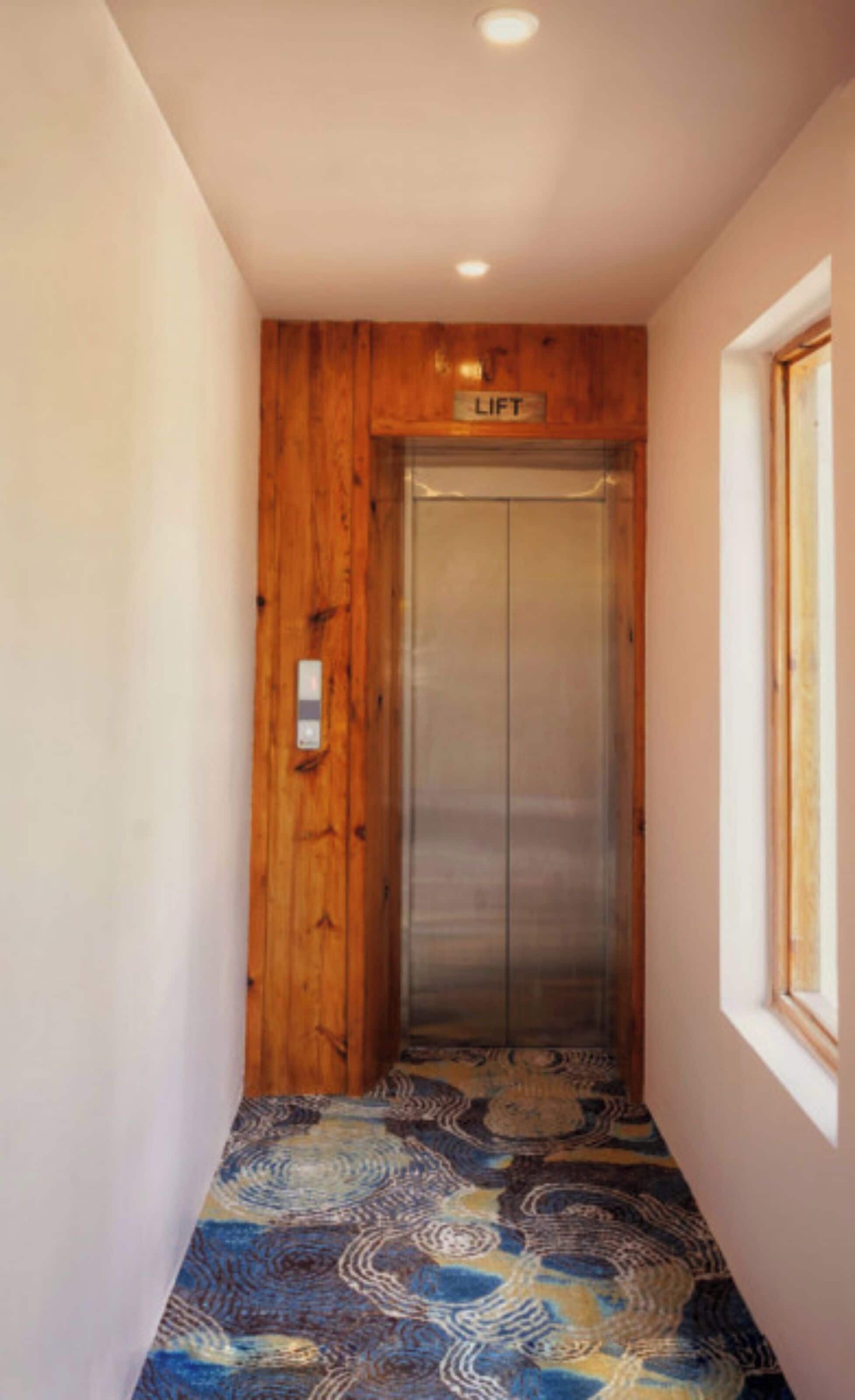 A narrow hallway with a wooden wall, a lift, and patterned flooring.