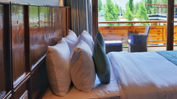 Un dormitorio con una cama grande, cabecera de madera y vistas a un balcón con mobiliario exterior.