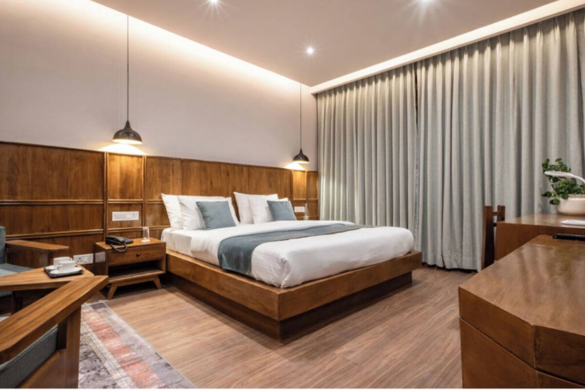 Una habitación de hotel moderna con una cama de madera, mesitas de noche, un escritorio y un amplio ventanal con cortinas.