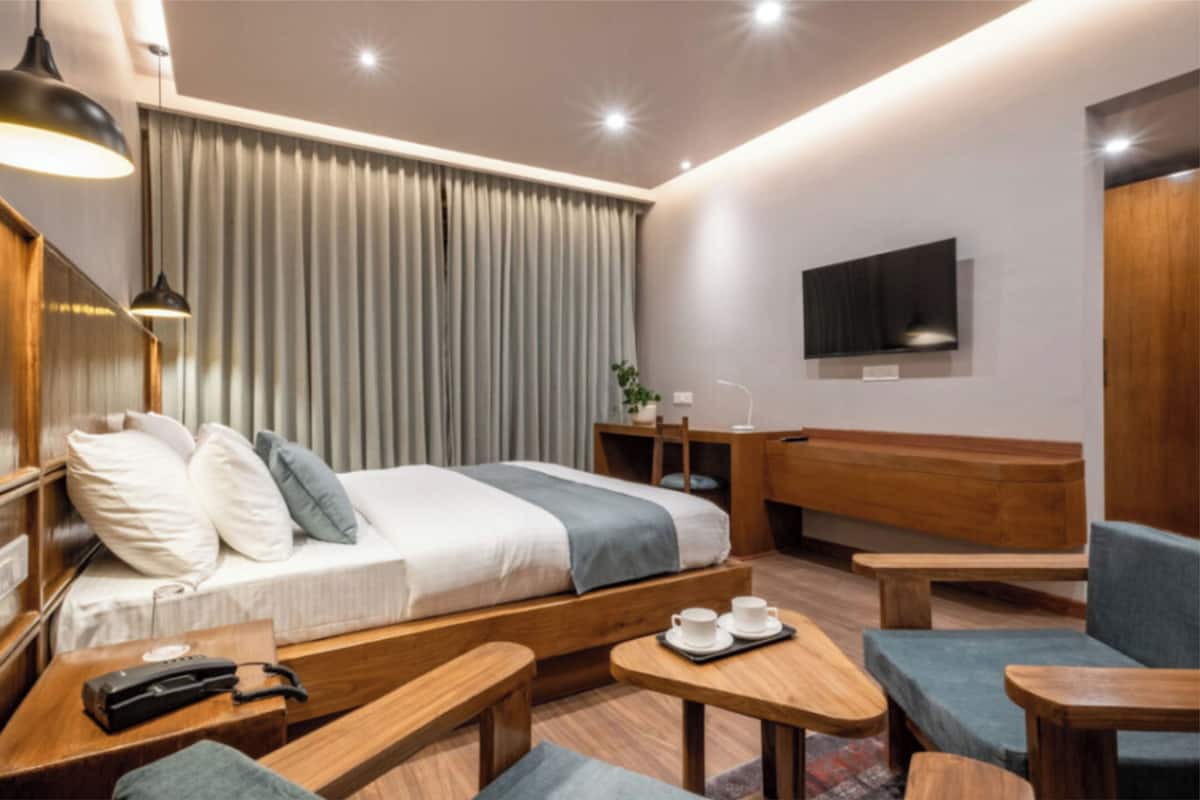 Una habitación de hotel moderna con cama, muebles de madera, un escritorio, una silla, televisor y ventana con cortinas.