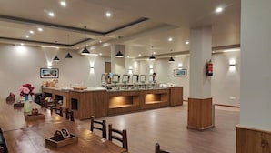 Un comedor moderno con una mesa y sillas de madera, una zona de bar central con varios mostradores, iluminación colgante y un extintor en la pared.