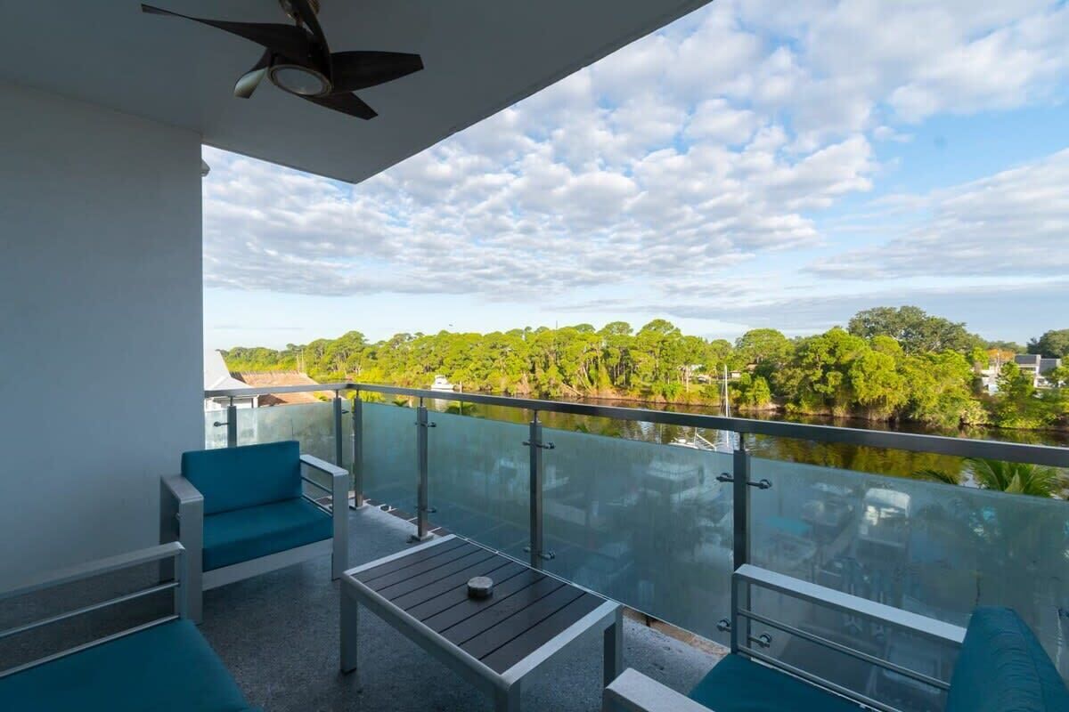 A balcony with a glass railing, a ceiling fan, and a view of a river and greenery.