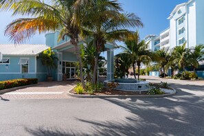 A hotel entrance with a covered walkway, palm trees, and a circular water feature. - Portside Suite - Cape Crossing Resort and Marina (Merritt Island)