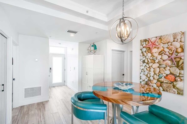 Un comedor moderno con una mesa de vidrio, sillas color turquesa, una lámpara colgante y una pared con un mural de caracoles y estrellas de mar.