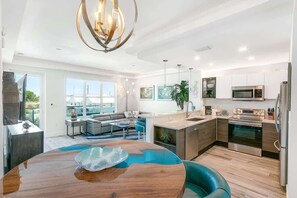 Una cocina moderna con electrodomésticos de acero inoxidable, un comedor con mesa de madera y una sala de estar con sofá y ventanas amplias.