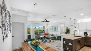 A modern kitchen with a central island, a dining area with a wooden table, and a living room with a sofa and coffee table.