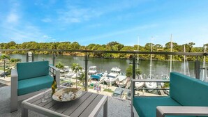 A balcony with a view of a marina, a table with a bottle and glasses, and two teal chairs.