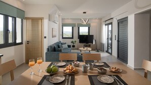 A modern living room with a sofa, TV, and dining area with a table set for breakfast. - Pura Vida Villa, 2 Heated Pools, Hot Tubs & Sauna (Rethymno)