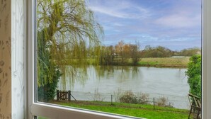 Vista de un río con un sauce, una cerca y una zona cubierta de césped.