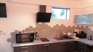 Eine kleine Küche mit Mikrowelle, Toaster und Spüle. Über der Spüle befindet sich ein Fenster und eine flache Bildschirmfernseher ist an der Wand montiert.