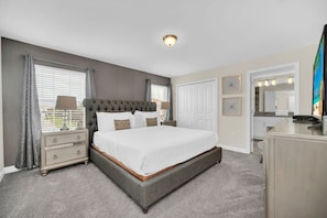 A bedroom with a large bed, bedside tables, a dresser, a mirror, and a window with curtains.
