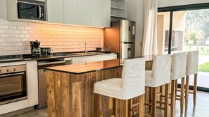 Een moderne keuken met witte kasten, een houten eiland, barstoelen en een uitzicht op de omgeving door grote ramen.
