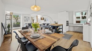 Eine moderne Küche mit weißen Schränken, einem Essbereich mit einem Holztisch und einem großen Fenster, das natürliches Licht hereinlässt.