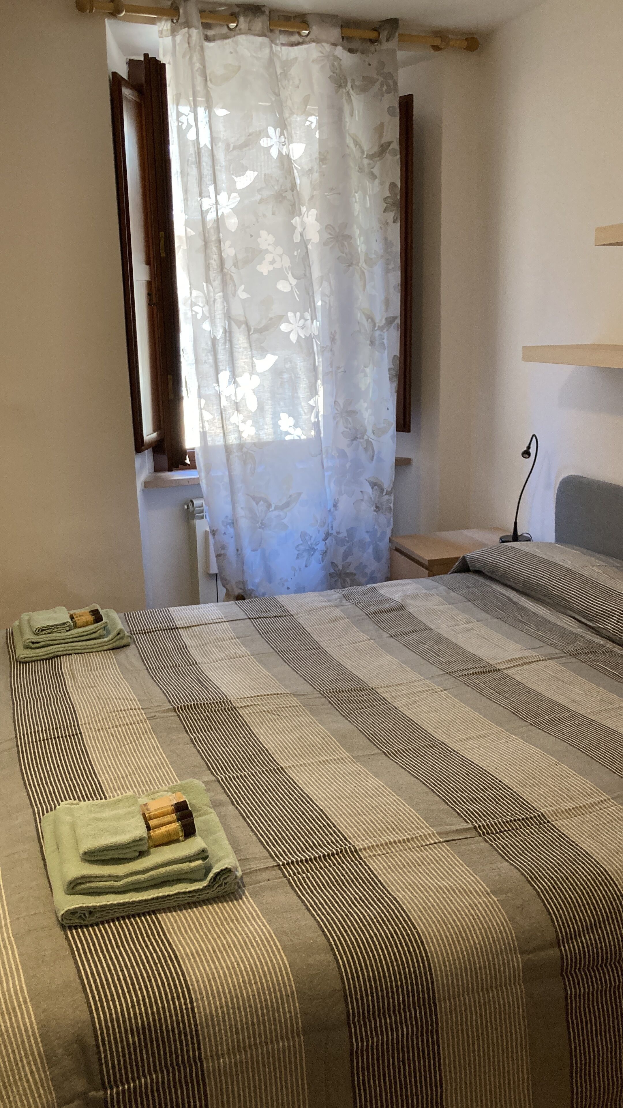 Ein Hotelzimmer mit einem Bett, einem kleinen Tisch, einem Stuhl und einem Fenster mit blumigen Vorhängen.