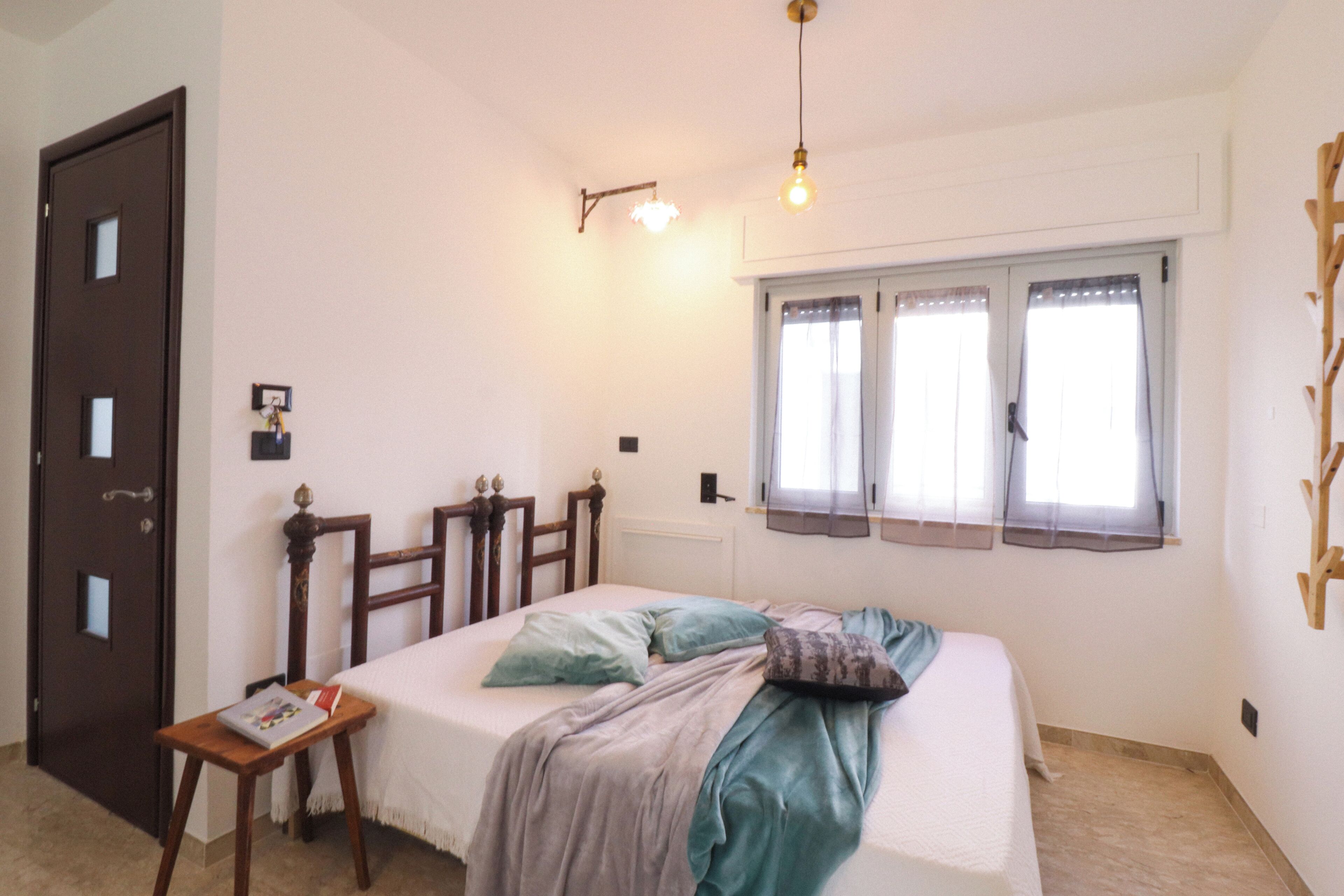 A bedroom with a bed, bedside table, and a window with curtains.