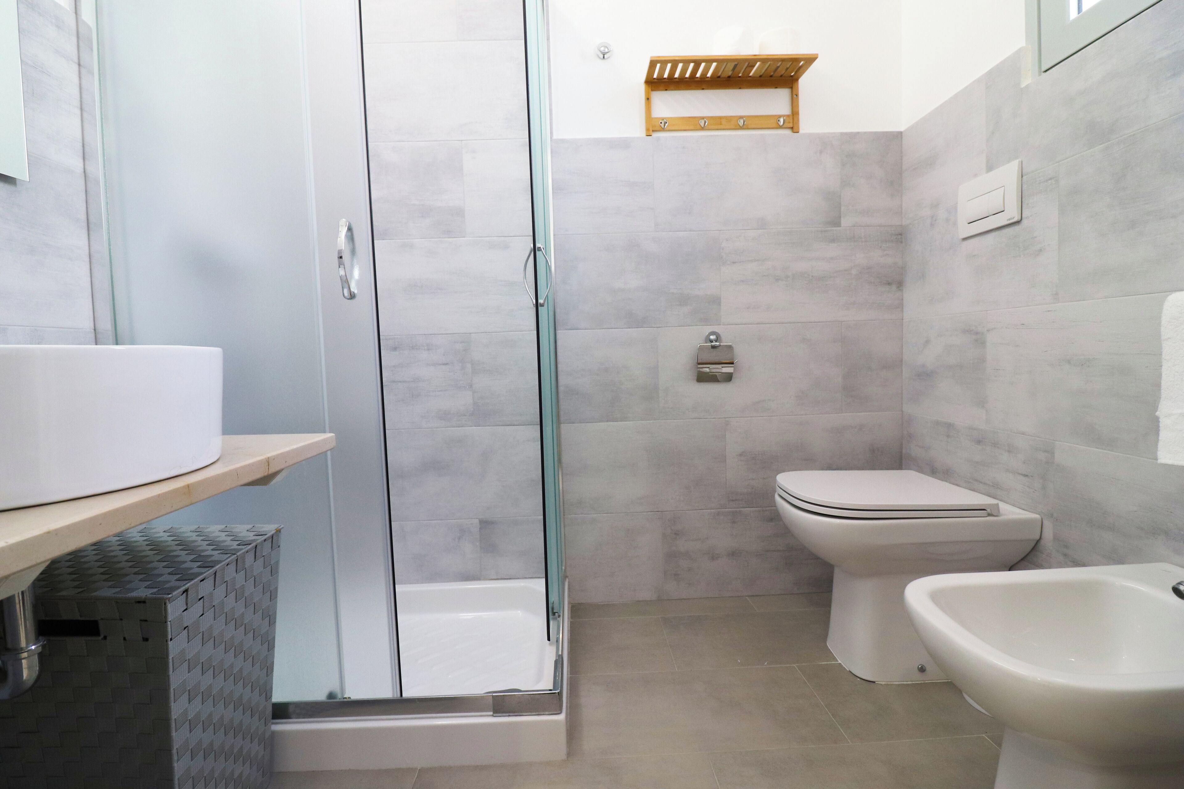 A modern bathroom with a glass-enclosed shower, a toilet, a bidet, and a sink.