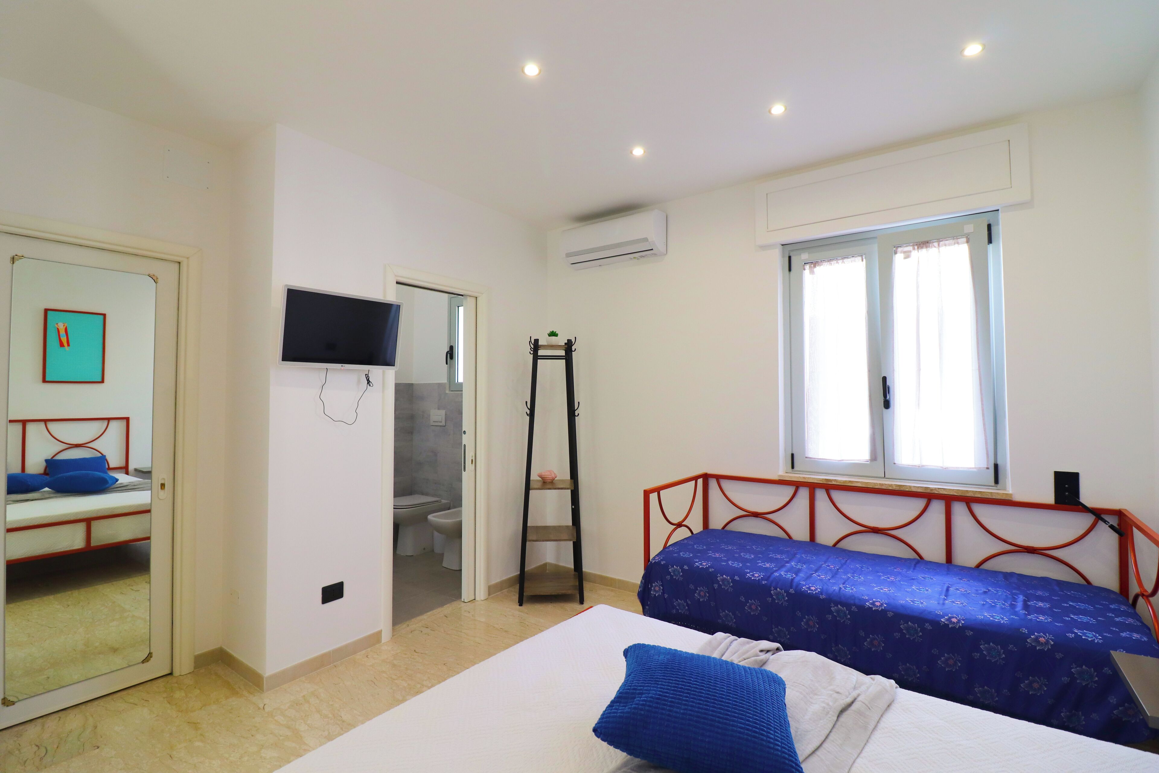 Quarto com cama, espelho, televisão e janela.