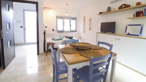 A modern kitchen with a wooden table, blue chairs, and a TV on a shelf. - Casa Malika Space, Comfort & Mediterranean Charm in the Heart of Otranto (Otranto)