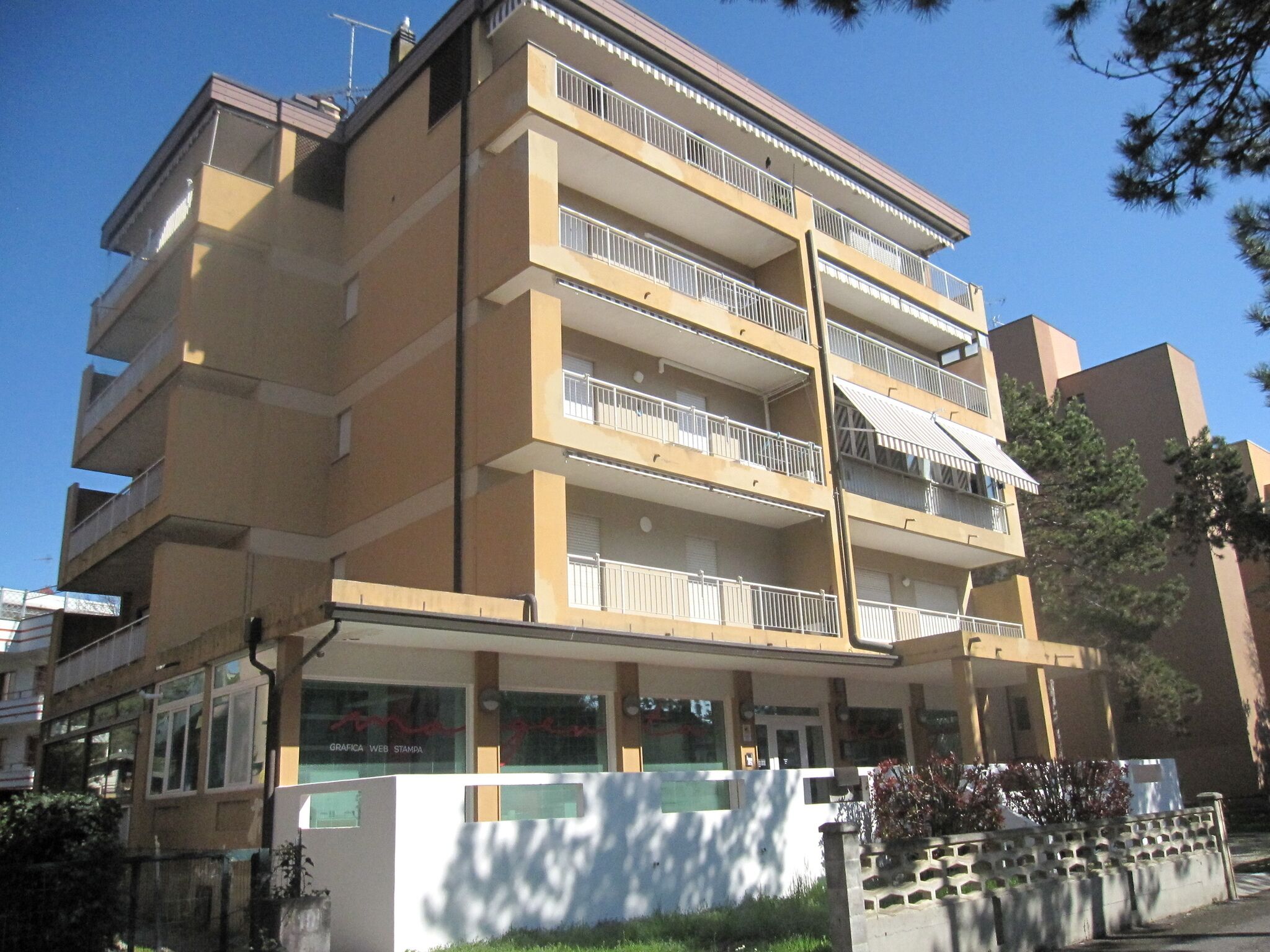 Un edificio de varios pisos con balcones, una entrada a nivel de calle y una señal visible.
