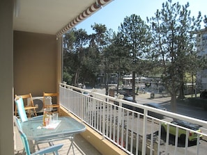 Ein Balkon mit Tisch, Stühlen, Geländer und Blick auf Bäume und Gebäude.