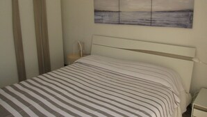 A bedroom with a bed, a nightstand, a wall-mounted painting, and a window with curtains. - Enjoy the sun From our Lovely Terrace (Grado)