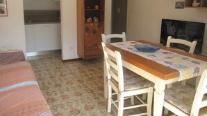 A dining area with a wooden table and white chairs, a kitchen in the background, and a patterned floor. - Enjoy the sun From our Lovely Terrace (Grado)