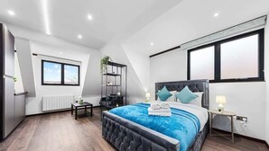 A modern bedroom with a large bed, a small table, a chair, a radiator, and a window.