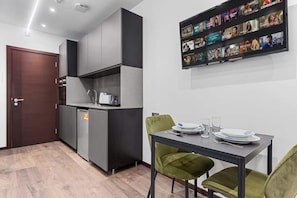 A compact kitchen with modern appliances, a dining area with a table and chairs, and a wall-mounted TV displaying various channels.