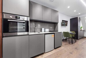 A modern kitchen with stainless steel appliances, grey cabinetry, and a dining area with a table and chairs.