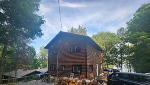 A log cabin with a gravel driveway and stacked firewood. - Discover Serenity: Ultimate Summer Getaway Awaits at Charming Cottage Retreat! (Bancroft)
