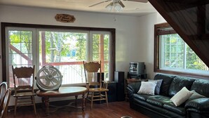 A room with a wooden floor, a ceiling fan, a wooden staircase, a green sofa, and a dining table with chairs. - Discover Serenity: Ultimate Summer Getaway Awaits at Charming Cottage Retreat! (Bancroft)
