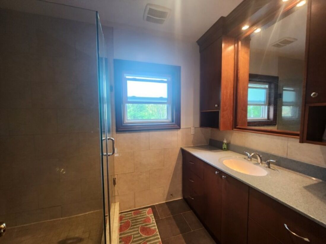 Een badkamer met een douchecabine van glas, een wastafel met spiegel en een raam boven de wastafel.