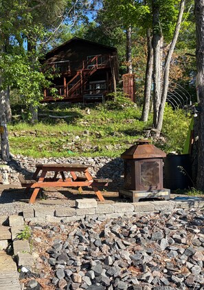 En rustik stuga med en träveranda och en trappa, omgiven av träd och en gång av sten.