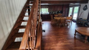 A spacious kitchen with wooden cabinets, a dining area with a round table and chairs, and a wooden staircase. - Discover Serenity: Ultimate Summer Getaway Awaits at Charming Cottage Retreat! (Bancroft)