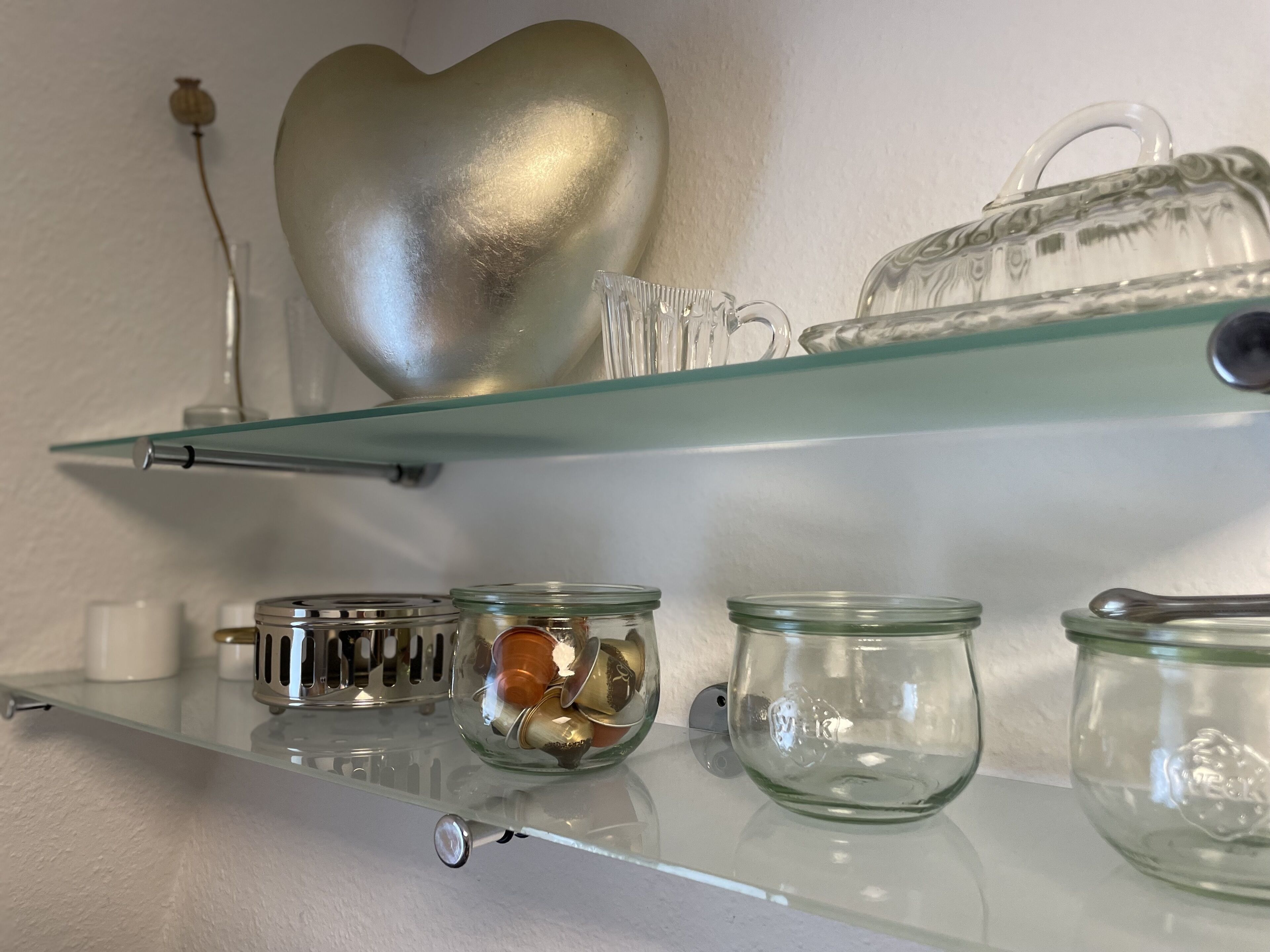 A glass shelf with decorative items including a heart-shaped object, a crystal jug, and several glass jars.