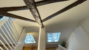 Une pièce de style « loft », avec des poutres en bois apparentes, un escalier, un canapé et une petite table.