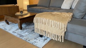 Un salon moderne avec un canapé gris, une table basse en bois et un plaid beige.