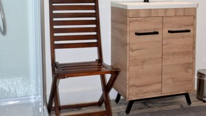 Un baño con una silla de madera, un lavabo con espejo y una zona de ducha.