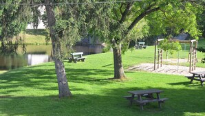 Un parque con mesas de picnic, un conjunto de columpios y un estanque.