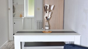 Una cocina moderna con muebles blancos, una pared de acento de madera y un área de comedor con un banco y un jarrón de ramas secas.