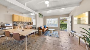 A spacious kitchen with wooden cabinets, a dining area with a table and chairs, a living room with a sofa and coffee table, and a large window with a view of the outside.