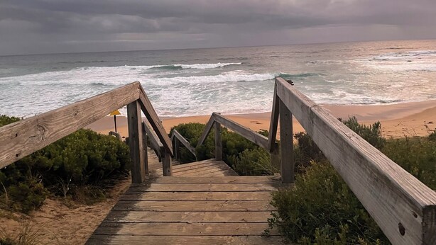 Un escalier en bois menant à une plage, avec les vagues de l’océan en arrière-plan.