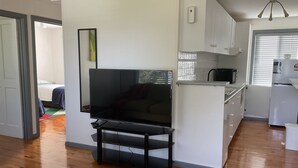 Un espace de vie compact comprenant un téléviseur posé sur un meuble, un coin cuisine et un plancher en bois.