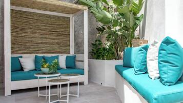 A modern outdoor seating area with a sofa and two small tables, surrounded by large green plants and a bamboo wall.