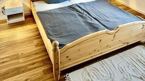 Ein hölzernes Bett mit grauer Decke und Kissen, zwei Nachttische mit Lampen und ein Holzboden.