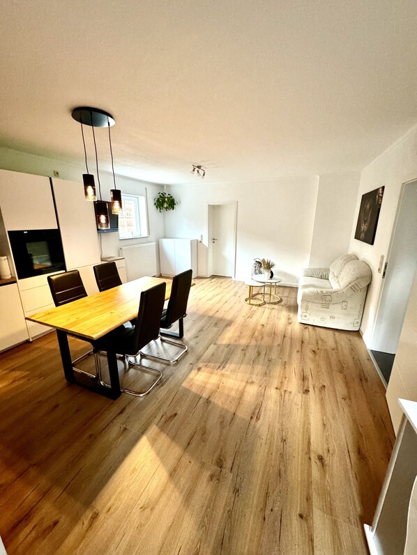 Una cocina moderna con suelo de madera, una mesa de comedor con sillas e iluminación colgante.