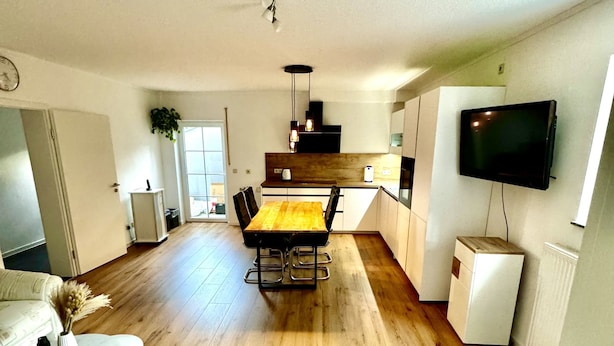 Ein moderner Wohnraum mit Holzboden, einem Essbereich mit gelbem Tisch und einer Küche mit an der Wand montiertem Fernseher.