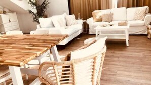 A modern living room with a wooden dining table, white sofas, and a wicker chair. - Atemberaubende Villa Palmeral in Corralejo mit Whirlpool & Beheizten Privatpool (La Oliva)