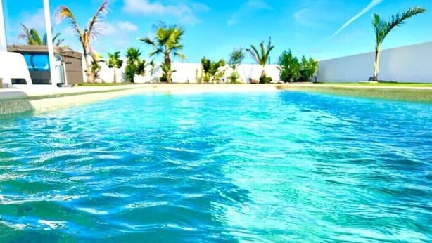 A clear blue pool surrounded by palm trees and a white building. - Atemberaubende Villa Palmeral in Corralejo mit Whirlpool & Beheizten Privatpool (La Oliva)