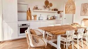 A modern kitchen with white cabinetry, a wooden dining table, wicker chairs, and a hanging light fixture. - Atemberaubende Villa Palmeral in Corralejo mit Whirlpool & Beheizten Privatpool (La Oliva)